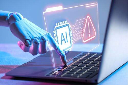 Robotic hand interacting with a laptop, holographic AI chip and a red warning icon signaling an AI security alert.