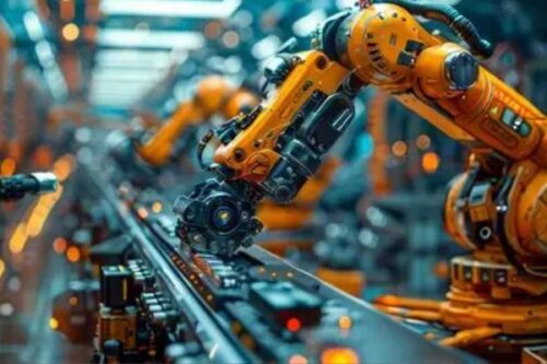 Industrial robots in orange attach and manipulate parts on a moving conveyor belt in a high-tech factory.