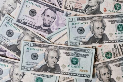 Pile of overlapping US dollar bills of various denominations on a surface, showing scattered cash.